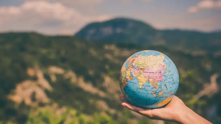 A person holding a globe in front of a mountain view